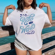 Searching for the ultimate beach vibe? Whether you're dreaming of a Ride the Wave Tshirt, Summer Beach Shirt, Surf Tshirt Design, Surf Graphic Tee, Beach Vibes, Summer Waves, Beach Summer Apparel, or Beach Vacation Tshirt, we've got you covered. ---- Unisex Size and Material ----  This classic unisex jersey tee feels like an instant favorite. Crafted from soft cotton with a high-quality print, it's designed for lasting comfort and style. Featuring ribbed knit collars, tapered shoulders, and rein Blue Summer T-shirt For Surfing, White T-shirt For Beach Vacation, White T-shirt For Beach, White Beachy Surfing Top, White T-shirt For Summer Beach Season, Short Sleeve T-shirt With White Print For Beach, White Beachy Tops For Surfing, White Beachy Top For Surfing, White Print Short Sleeve T-shirt For Beach