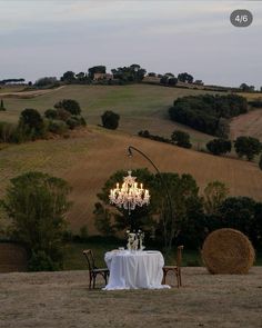 a table set for two in the middle of a field with a chandelier