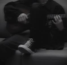 a person sitting on a couch with a guitar in their hand and wearing converse shoes