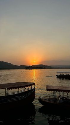 two boats sitting in the water at sunset