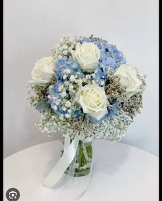 a bouquet of white and blue flowers in a glass vase with ribbon on the side