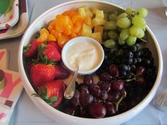 a bowl filled with grapes, strawberries, oranges and yogurt next to other fruit