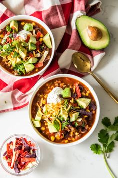 two bowls of mexican soup with avocado and sour cream on the side next to it