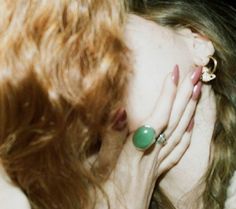 a close up of a person with red hair and rings on her head, holding their hand to her face