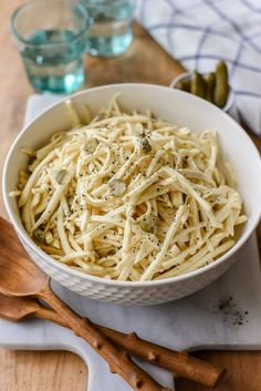 a white bowl filled with pasta sitting on top of a table next to two wooden spoons