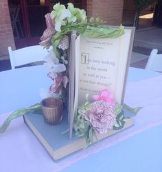 an open book sitting on top of a table next to a vase with flowers in it