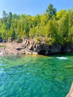 a body of water surrounded by green trees and rock formations in the middle of it