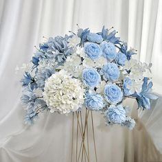 a bouquet of blue and white flowers in a vase on a table next to a curtain