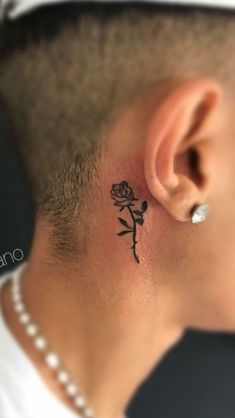 a man with a small rose tattoo on his left side behind the ear is wearing a pearl necklace