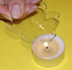 a woman's hand holding a lit candle in front of a small glass vase