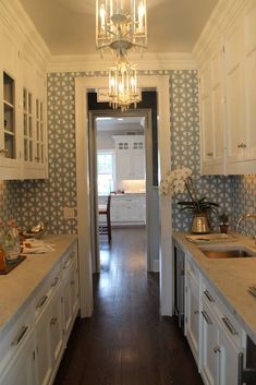 a long narrow kitchen with white cabinets and blue wallpaper on the walls, along with a chandelier hanging from the ceiling