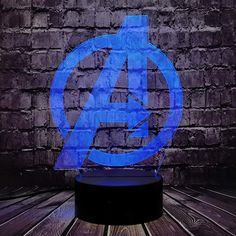 the avengers logo is illuminated in blue on top of a wooden table next to a brick wall