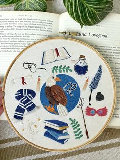 a hand holding a cross stitch book with an embroidered bird and books on the cover