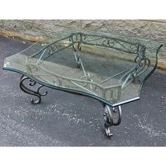 a glass coffee table with wrought iron legs and an intricately designed design on top