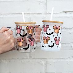 two people holding coffee cups with bats and pumpkins on them, one has a straw in it