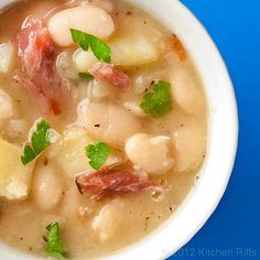 a close up of a bowl of soup with beans and ham in it on a blue surface