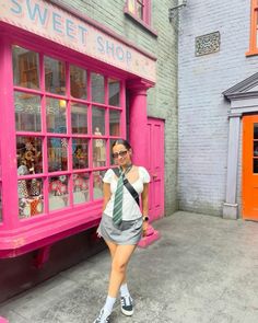 a woman is standing in front of a pink store with an odd tie on her neck