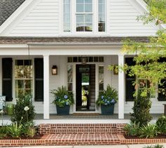 a white house with black shutters and flowers on the front porch, along with potted plants