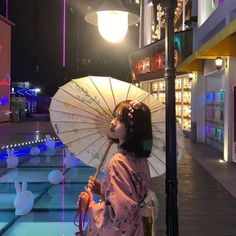 a woman holding an umbrella standing next to a lamp post in front of a building