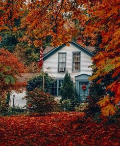 a white house with an american flag in front of it surrounded by fall leaves and trees