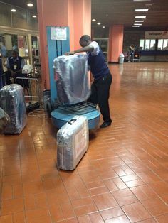 a man unloading luggage on top of a blue cart in an airport lobby with people standing around