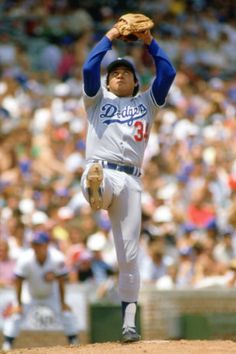 a baseball player pitching a ball on top of a field in front of a crowd