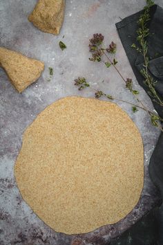 an uncooked pizza crust sitting on top of a table next to some herbs