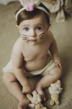 a baby is sitting on the floor with her face painted like a cat