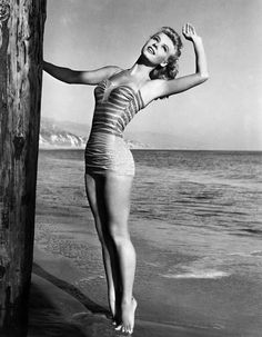 a woman in a bathing suit standing on the beach next to a pole and looking at the camera