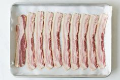 raw bacon strips lined up on a baking sheet