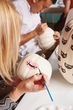 a man and woman decorating pumpkins with cat faces on them, sitting at a table