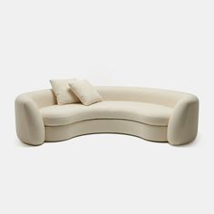 the curved sofa has two pillows on it and is made out of white fabric with a light colored finish