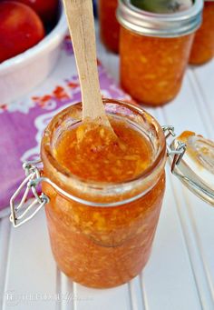 a wooden spoon in a glass jar filled with orange marmalade and peach jam