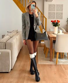 a woman is taking a selfie in her living room while wearing boots and holding a purse