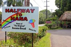 a sign for haleway to hanana in front of a road with palm trees