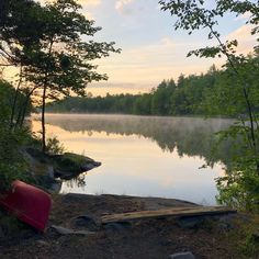 there is a canoe on the shore of this lake in the evening time, and it's still foggy