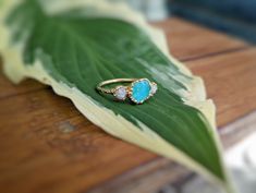 a gold ring sitting on top of a green leaf next to a white and blue stone