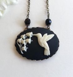 "Here is a super sweet hummingbird necklace featuring a nicely detailed cameo depicting a hummingbird with lily of the valley flowers. This cameo is black and white, it is horizontal style and set in an oxidized brass setting that is suspended from a nice quality non tarnish brass chain. You may select your desired chain length from the drop down menu. Handcrafted in the USA by Botanical Bird jewelry. Shipped in a lovely gift box and perfect for gift giving! Large Cameo Pendant measures: 1 1/4\" Black Cameo, Hummingbird Jewelry, Egyptian Necklace, Hummingbird Necklace, Lily Of The Valley Flowers, Hummingbird Pendant, Valley Flowers, Bff Necklaces, Flowers Black