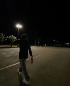 a man walking down the street at night with a can in his hand and an empty parking lot behind him