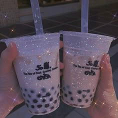 two people holding up plastic cups with liquid in them and sparkles on the ground