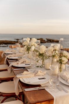 a long table set up with white flowers and place settings for dinner at the beach