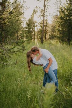 a man and woman kissing in tall grass with trees in the backgrouds