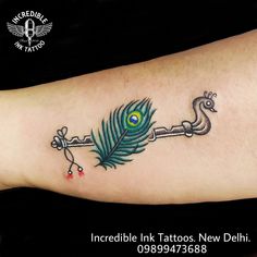 a peacock feather on the arm with a key tattoo