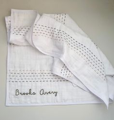 three white linens with embroidered words on them sitting next to each other, one folded and the other unwrapped