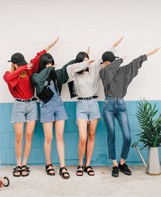 four people standing in front of a blue wall with their arms up and hands raised