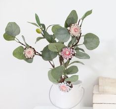 a white vase filled with pink flowers on top of a table