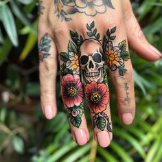 a woman's hand with flowers and a skull tattooed on the middle of it