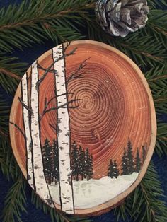 a painted wooden plate sitting on top of a blue table cloth next to pine cones