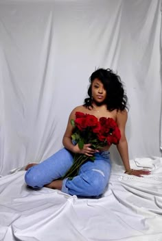 a woman sitting on the floor with roses in her lap and holding one red rose