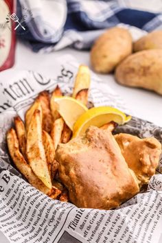 a basket filled with french fries and lemon wedges on top of a table next to potatoes